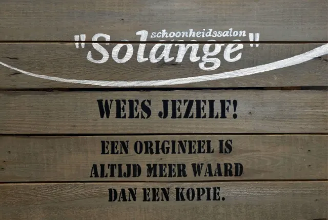 Houten bord in de salon met het logo en de tekst: Wees jezelf! Een origineel is altijd meer waard dan een kopie.